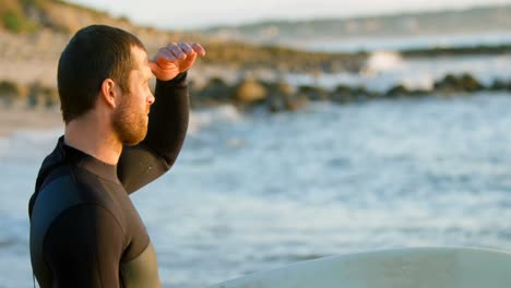 vista lateral de un surfista caucásico adulto con ojos protectoras mirando al mar en la playa 4k