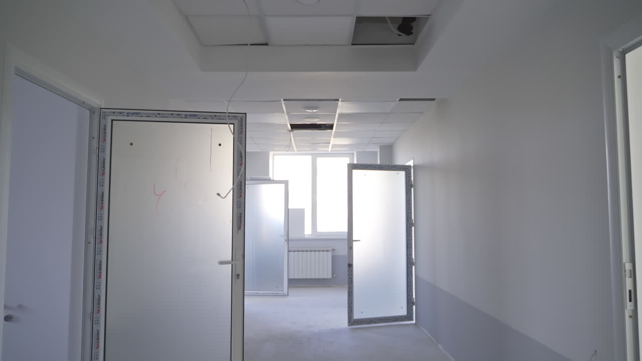 White corridor in a newly-built building. Focus on the unfinished pieces of ceiling cover. Open doors lock close up.