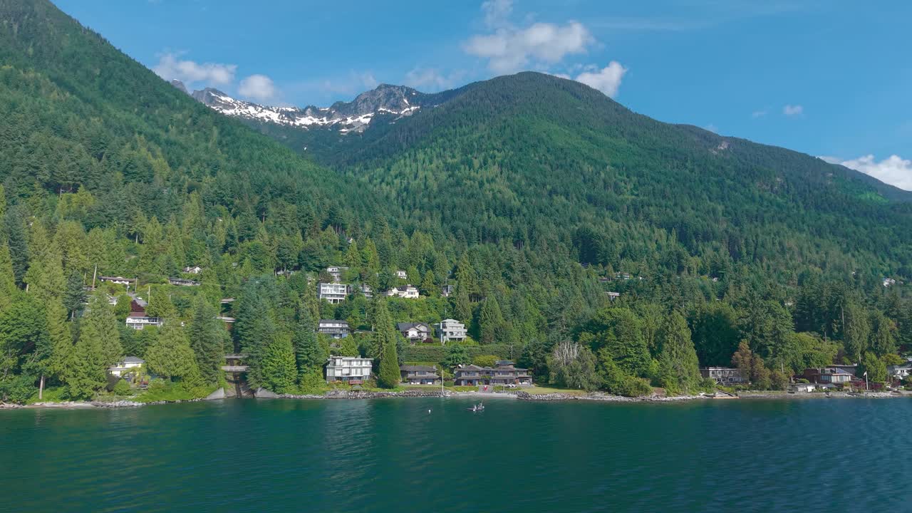 an aerial drone shot of luxury properties beneath Brunswick Mountains and along the coast of Lions bay with lush green trees all around