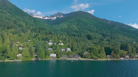 an aerial drone shot of luxury properties beneath brunswick mountains and along the coast of lions bay with lush green trees all around