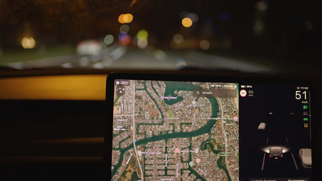 Car drives through city streets at night, illuminated by dashboard navigation and streetlights, interior view