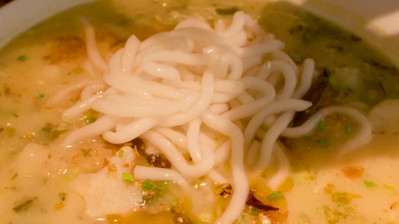 Primo piano di noodle di riso bianchi versati in brodo piccante con peperoncino e polpette di pesce