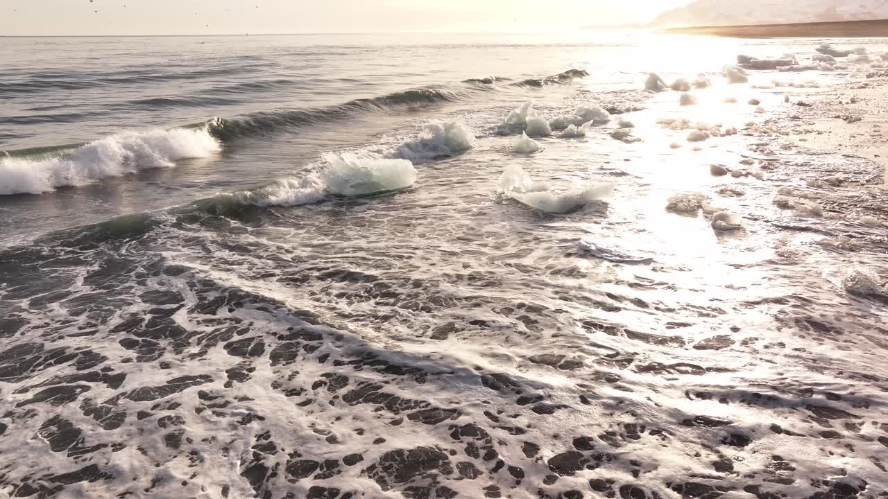 Ice chunks scatter along the shore as waves roll in on Iceland’s black sand beach