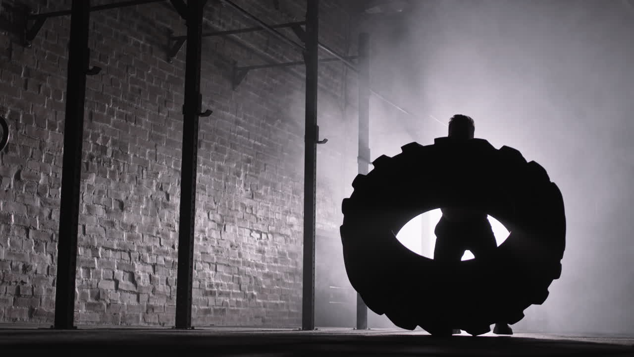 Sportsman Flipping Tire in Darkness in Gym