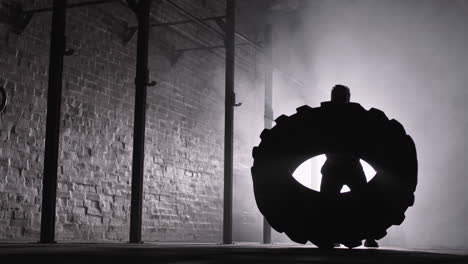 sportsman flipping tire in darkness in gym