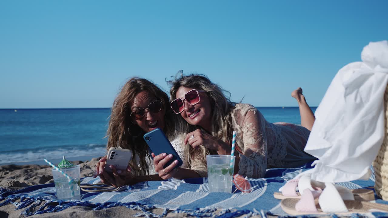Two Women Relaxing on the Beach with Drinks and Smartphones