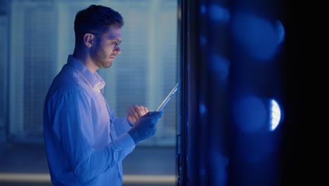 it technician in data center digital server room controlling work of rack server cabinets with a tablet. professional server engineer at work.