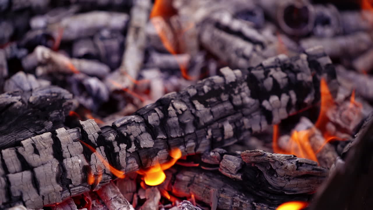 Texture of burned wooden logs in fire. Slight orange flame over the glowing wood. Close-up. Slow motion.