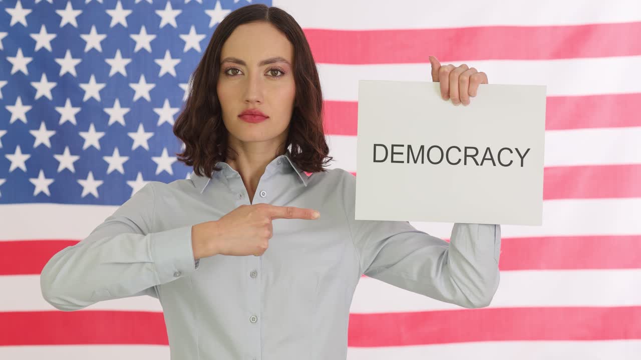 Woman holding 'Democracy' sign in front of American flag