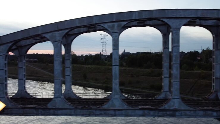 Vecchio ponte ferroviario in acciaio sopra un fiume circondato da prati, ripresa aerea laterale