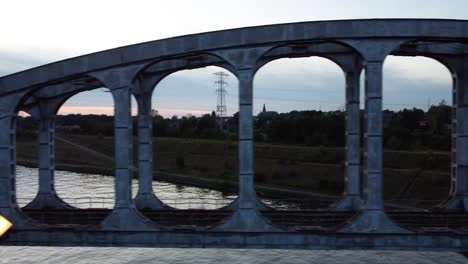 old steel railway bridge over river surrounded by meadows, aerial side fly