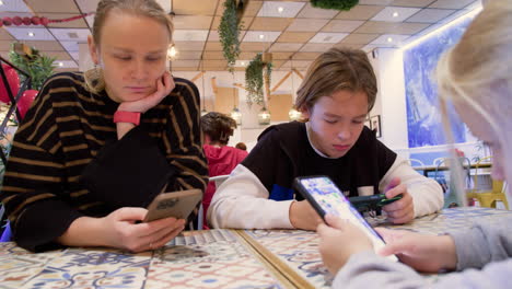 mamá y los niños están en sus teléfonos en un café - 2