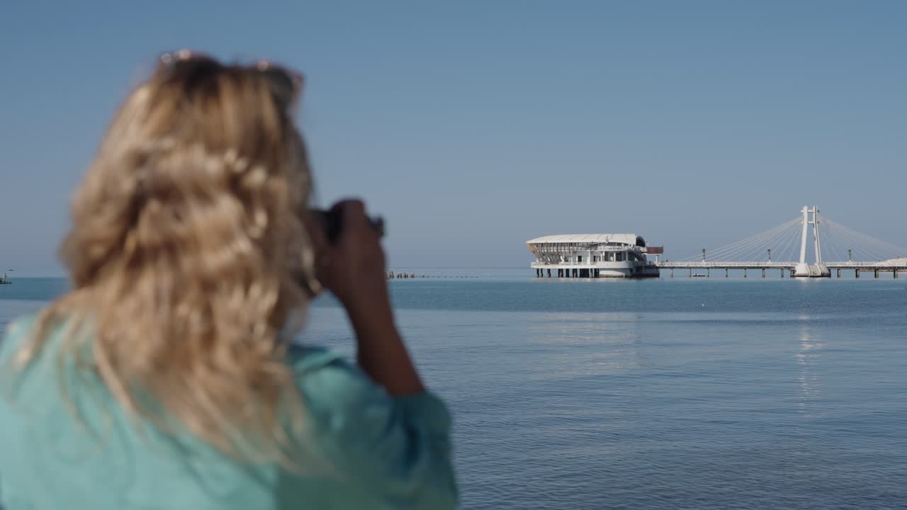 Caucasian female tourist with a camera filming the white building on the Adriatic Sea in Durres, Albania, wide shot