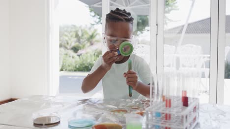 African-american-boy-sitting-at-table-holding-test-tubes-with-liquid,-in-slow-motion