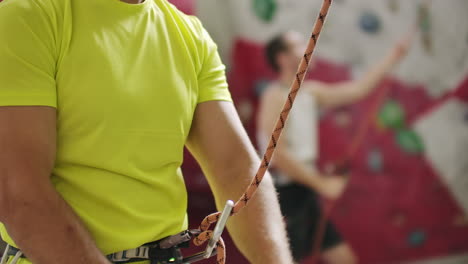 close-up of climber man belaying another climber against a wall with hooks in slow motion