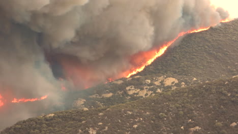 Large-red-hot-flames-crest-over-the-ridgetop-of-a-brush-covered-mountain-in-Hemet,-California