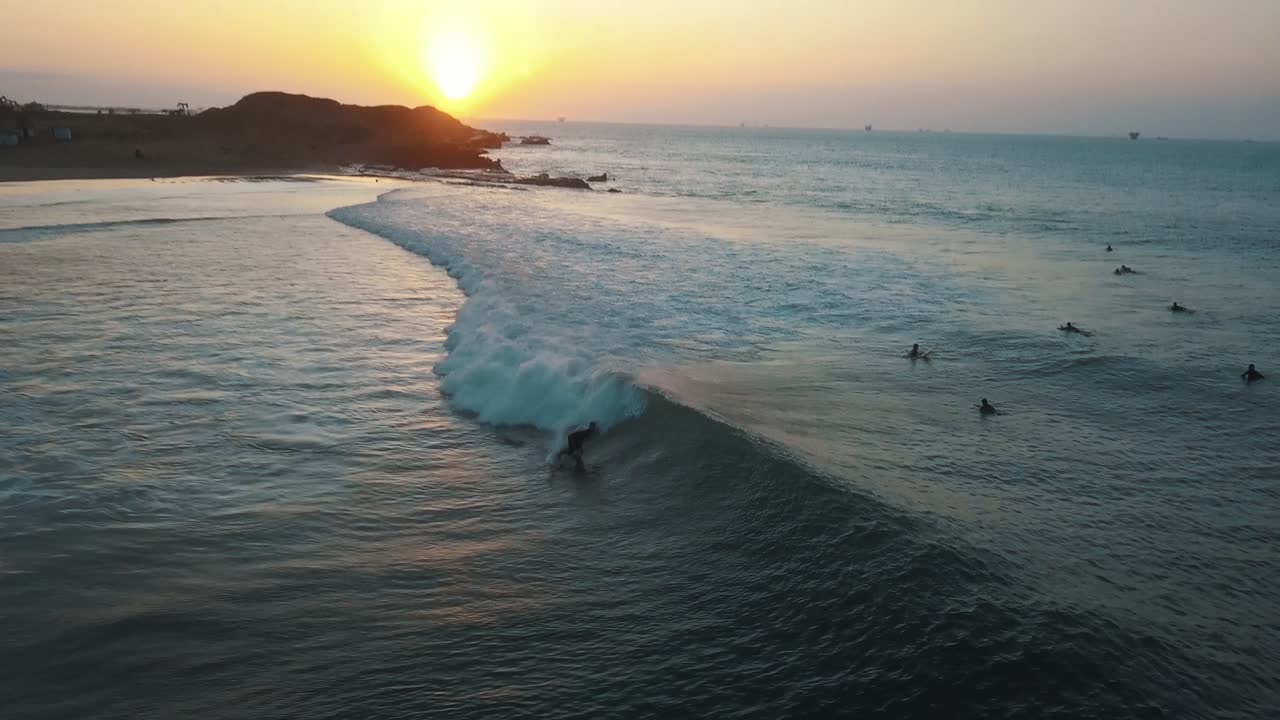 Aerial view surfing perfect waves during sunset, at the coast of Talara, in Peru - tracking, drone shot