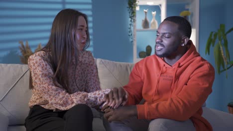 interracial couple sitting on sofa holding each other's hand and showing affection.