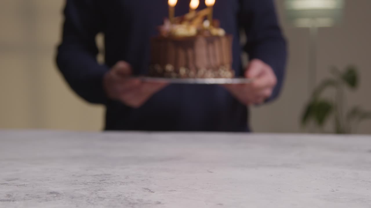 primer plano de una persona en casa que lleva un pastel de celebración de cumpleaños de chocolate decorado con velas encendidas