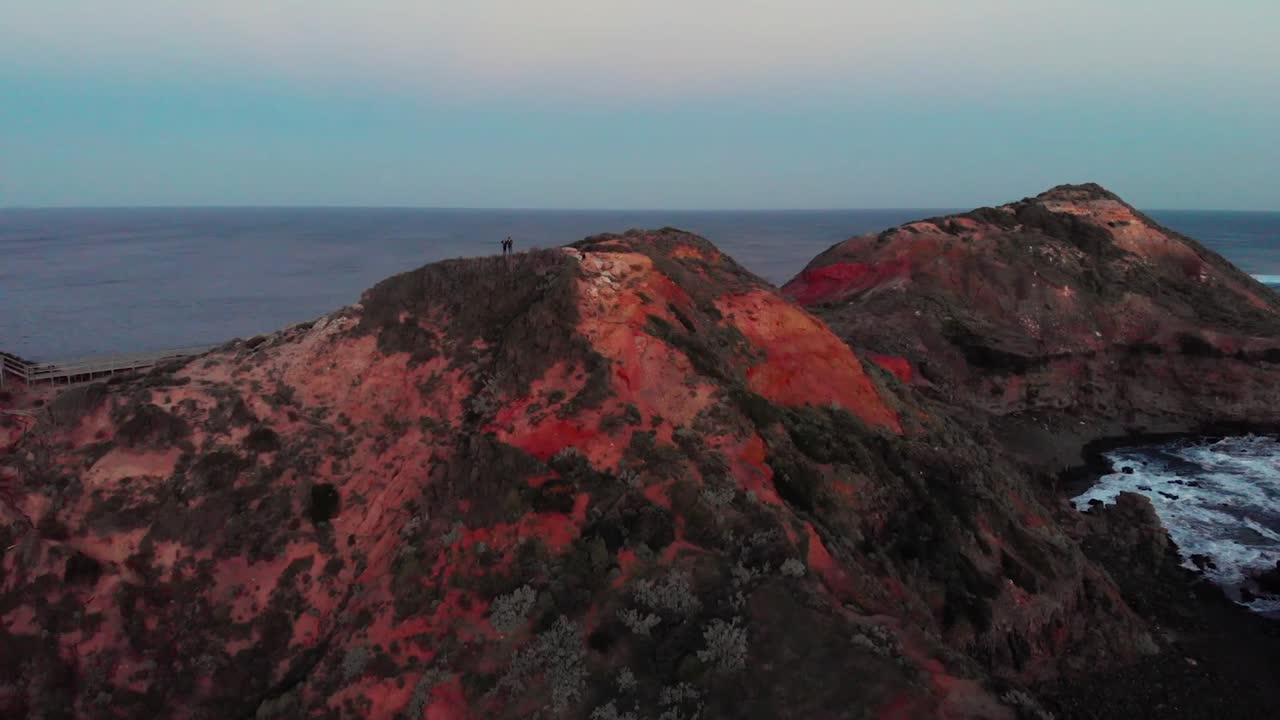 drone pull out of couple hiking over rocky coast line