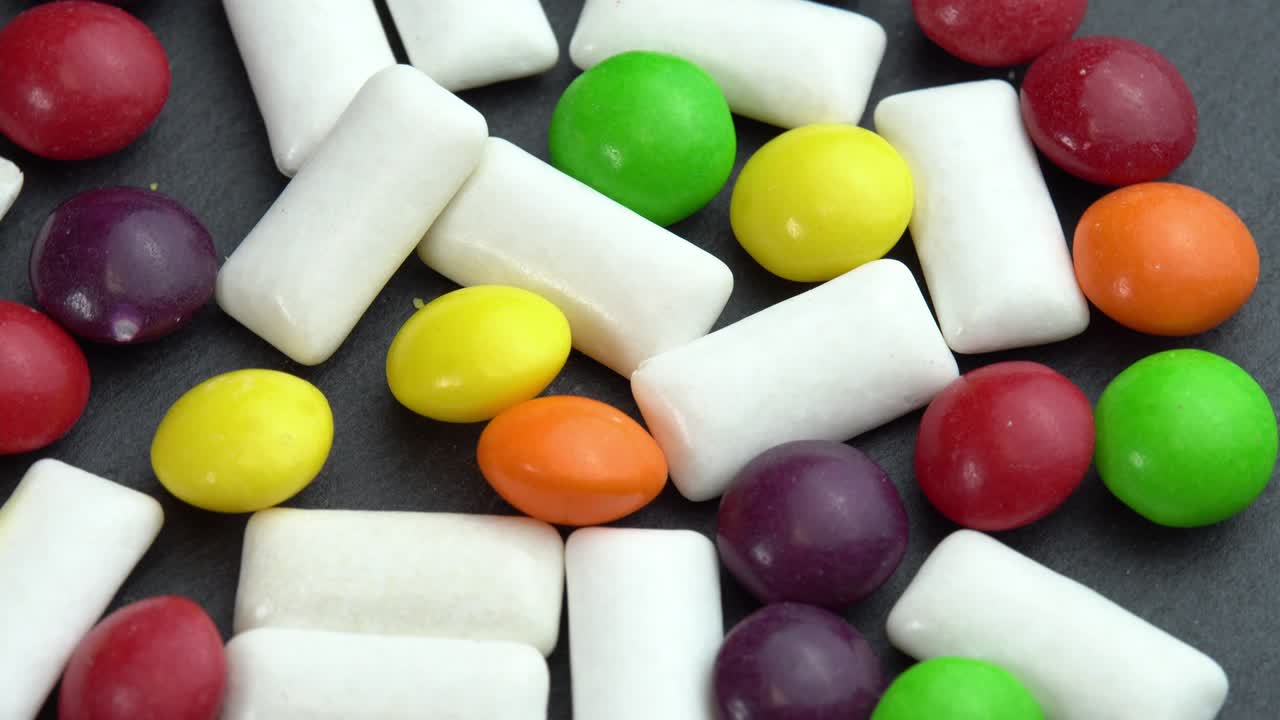dulces de colores dulces skittles y pastillas de mascar de menta, dulces de color giran en un plato negro