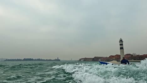 Low-angle-water-surface-view-of-Murano-lighthouse-seen-from-sailing-motorboat,-Italy