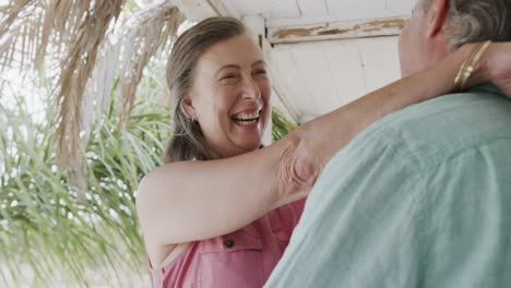 happy senior caucasian couple smiling and embracing on porch of beach house, in slow motion