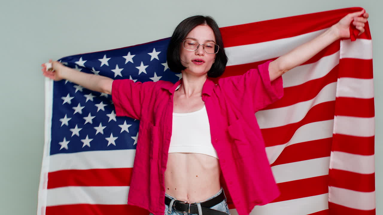 Giovane donna sventola con gioia la bandiera americana degli Stati Uniti con un sorriso che esprime patriottismo, sostegno, orgoglio ed emozione