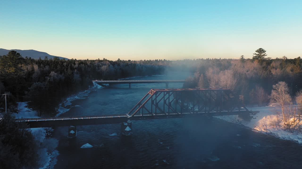 Aerial footage flying through the mist of a winter river past a railroad trestle and towards a bridge