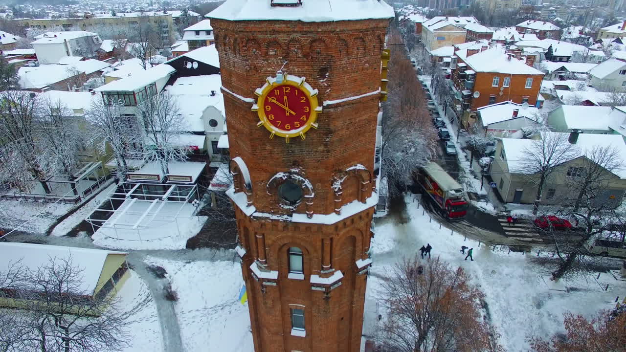 Historic building of old water tower with clock in Vinnytsia, Ukraine. Snow-covered roofs of the city in winter. Aerial view.