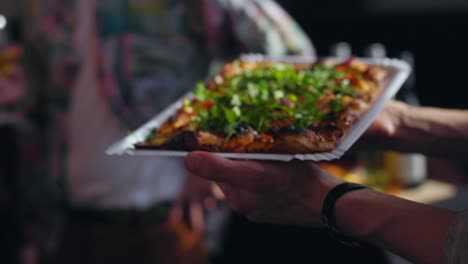 close up shot of a german baker holding a fresh baked flat bread pizza with arugula tomatoes and bread salad stone oven and gives it to guest 25 fps slowmotion