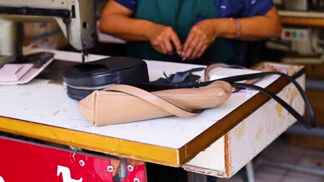 artisan skillfully sewing leather bags in a vibrant phuket workshop. bright lighting highlights detailed craftsmanship and traditional techniques