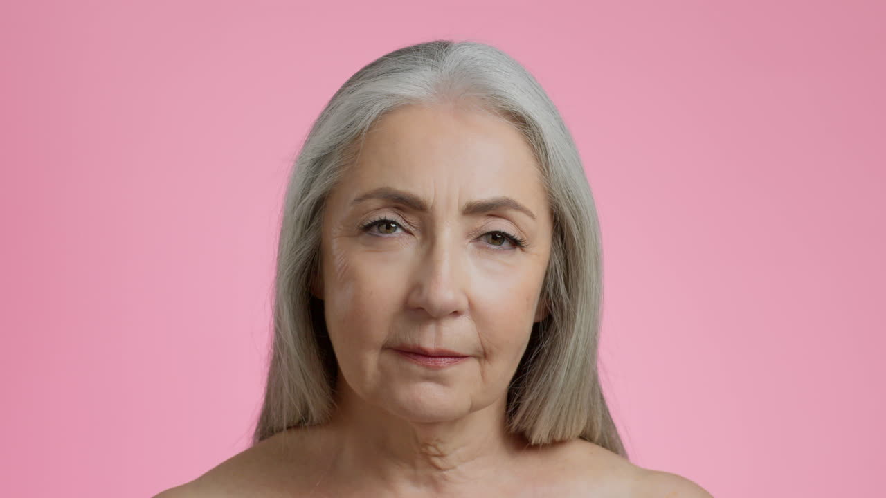 Close-up Portrait of a Senior Woman with Gray Hair on Pink Background