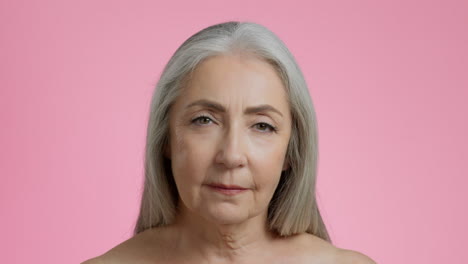 close-up portrait of a senior woman with gray hair on pink background