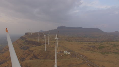 Eine-Langsame-Luftaufnahme-Einer-Stillstehenden-Windmühle-Mit-Sonnenuntergangshintergrund-Im-Hügeligen-Gelände-Indiens