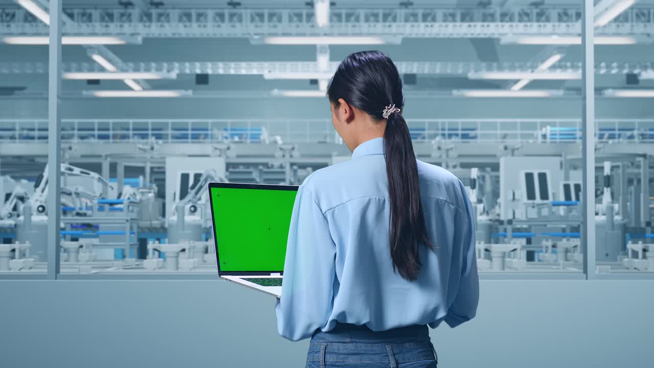 Back View Of An Asian Female Professional Worker Standing at Factory Digitalization for Innovative Project, Typing On Laptop'S Keyboard With Green Screen And Look At The Factory Once