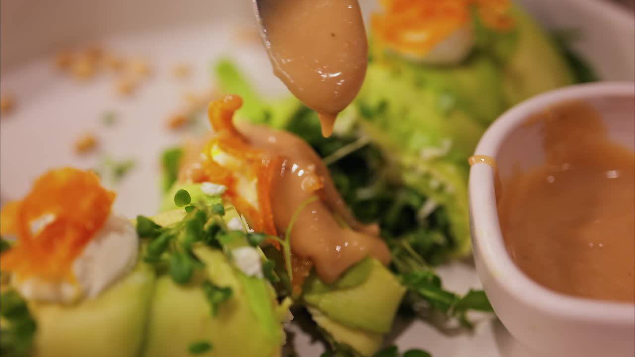 Close up of a woman pouring sauce on an avocado roll with sauce on a white plate at a restaurant
