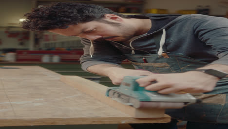 carpenter using belt sander in woodshop