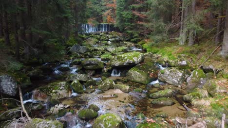 volando sobre el lecho de un río con rocas en un bosque en las montañas jizera, chequia