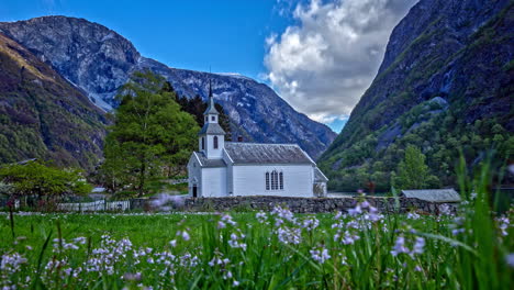 exterior view of bakka church on the shore of nærøyfjord surrounded by rocky mountains in aurland, norway with wildflowers in foreground