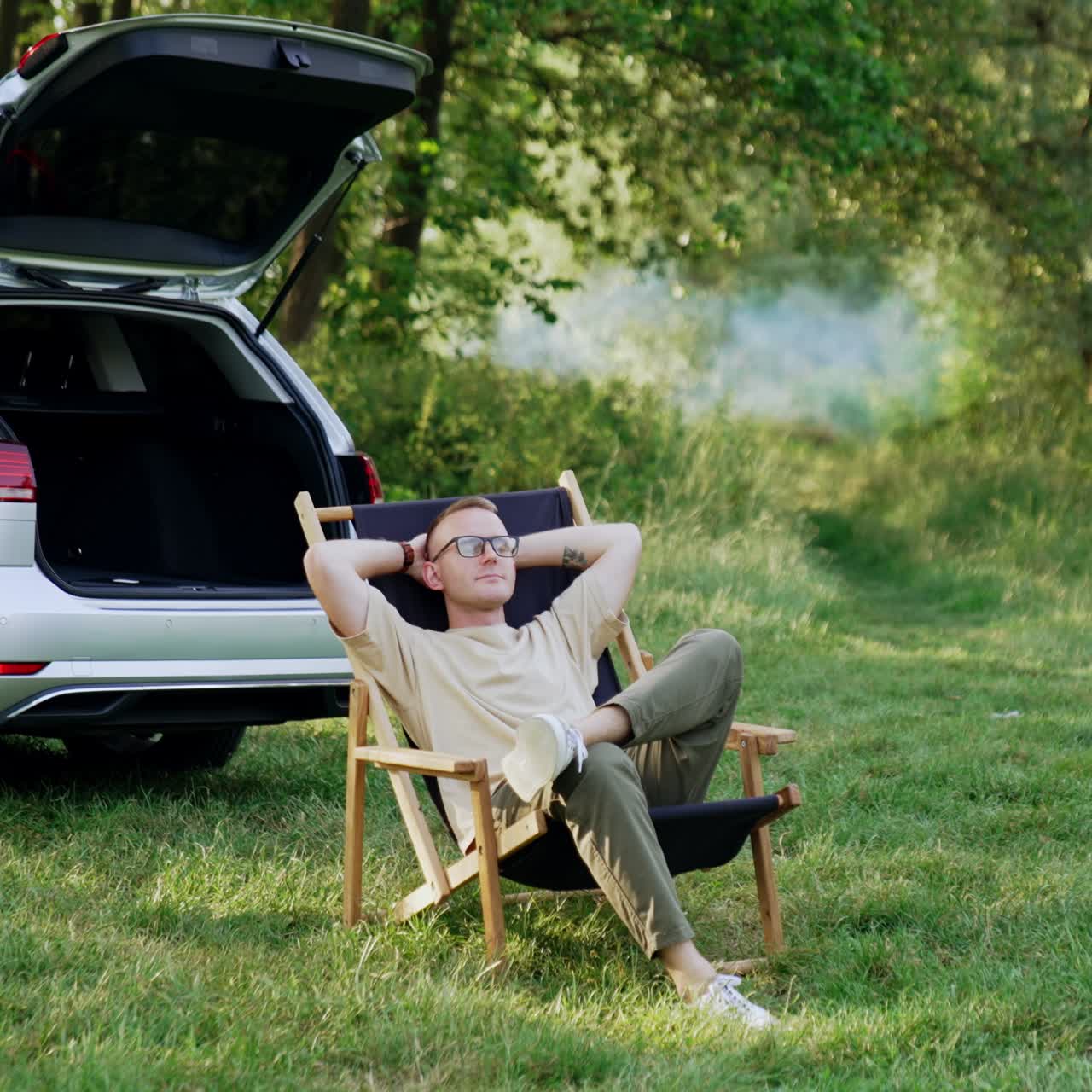 Man sitting comfortably in a folding chair stretches hands up. Summer relaxation in the wood