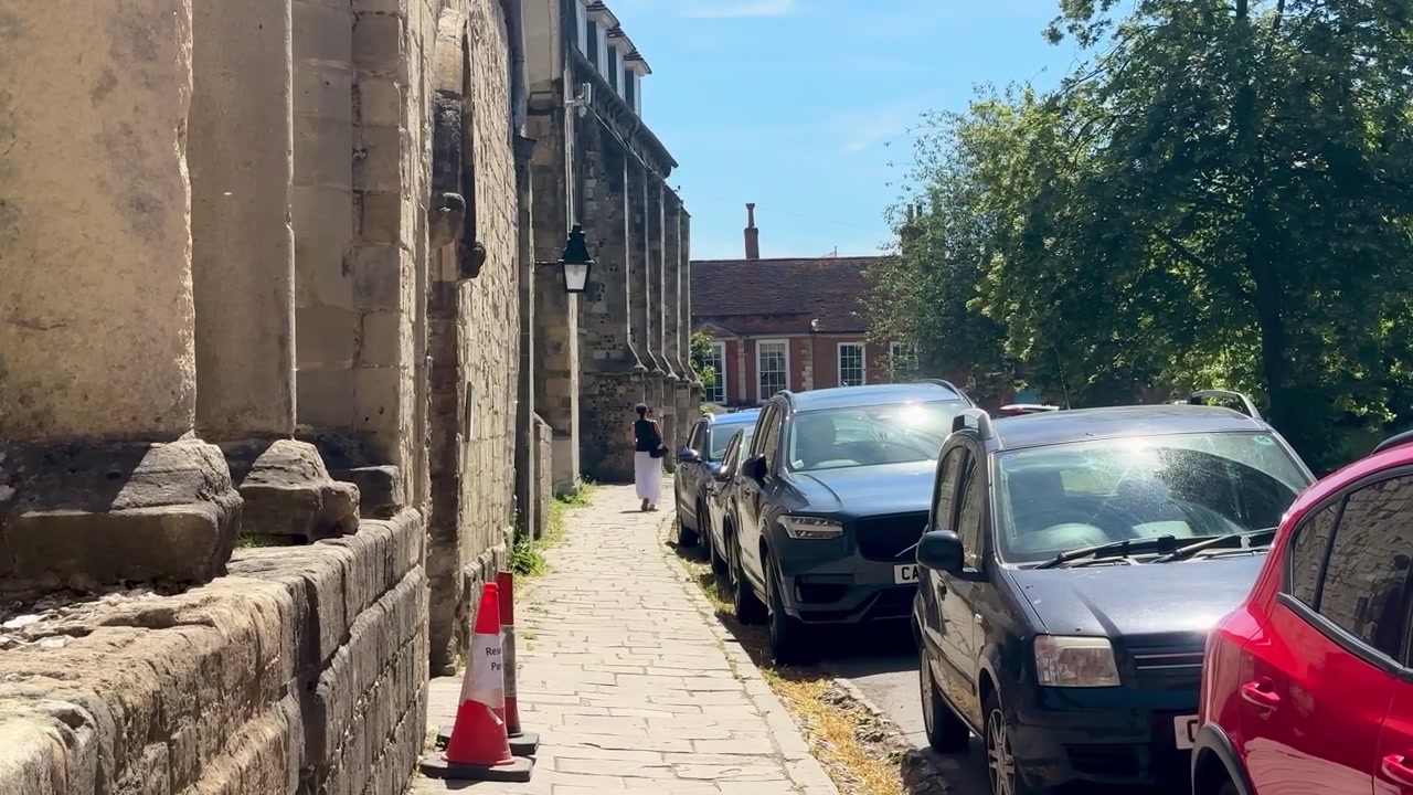 Sentiero in pietra accanto alla Cattedrale di Winchester, fiancheggiato da storici muri in pietra, auto parcheggiate ed edifici tradizionali a Winchester, Hampshire, Inghilterra.