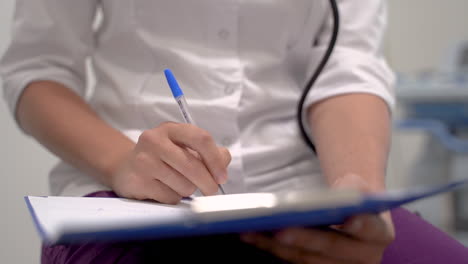 close up of the hands of a female doctor writing the symptoms and treatment of a patient