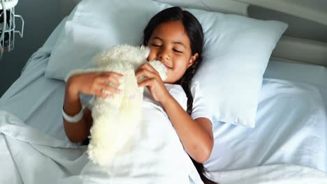 Smiling-girl-relaxing-on-bed-with-teddy-bear