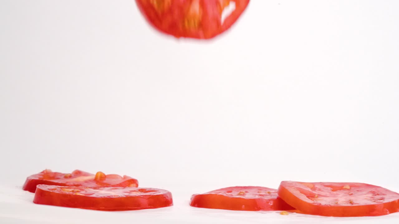 즙이 많은 밝은 빨간색 얇게 썬 토마토가 떨어지고 슬로우 모션으로 흰색 테이블 위에 있는 더미로 튀는
