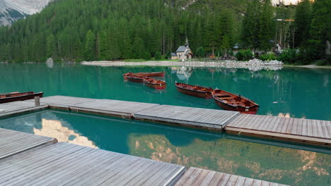 flying low across lago di braies at surise. drone video captures wooden rowboats and the historic boathouse with pristine reflections of the dolomites