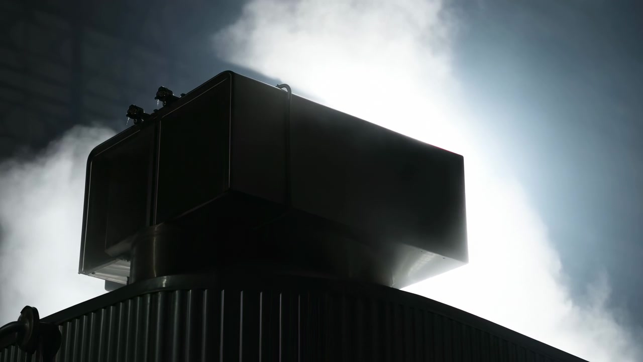 Un involucro metallico scuro e una tettoia ondulata rimangono fissi mentre il vapore illuminato si arriccia e cambia forma su uno sfondo luminoso, creando un contrasto elevato attorno a una rigida geometria industriale.