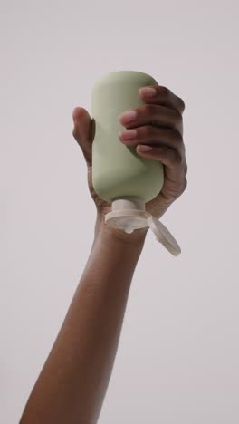 close up of woman squeezing bottle of beauty product until contents squirt out shot on white background