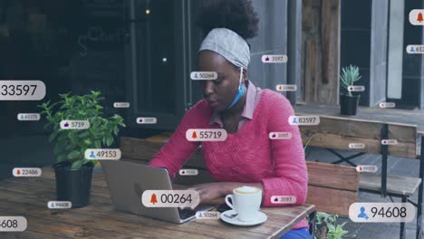 animation of social media icons over african american woman using laptop at a cafe
