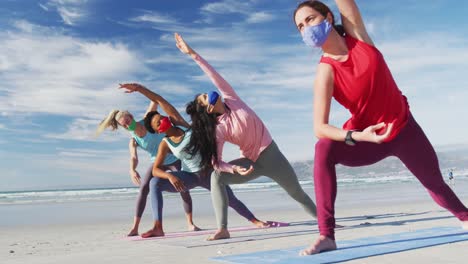grupo de diversas amigas con máscaras faciales practicando yoga en la playa